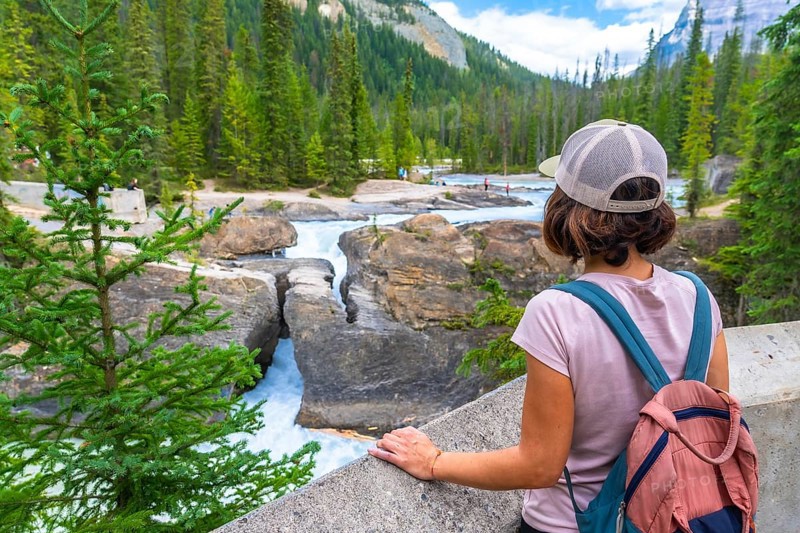 Female tourist with backpack enjoying the breathtaking view of the bow river natural bridge, a stunning rock formation in banff national park on a sunny summer day