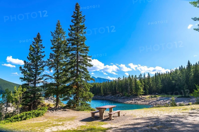 Breathtaking summer view of lake minnewanka, featuring turquoise waters, lush evergreen forests, and rugged mountains, creating an idyllic spot for relaxation in banff national park