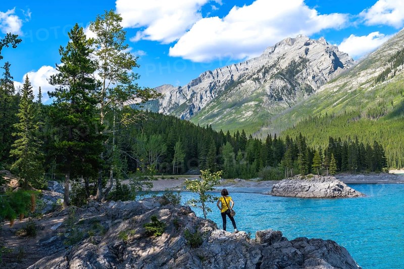 Tourist standing on rocks by the turquoise waters of lake minnewanka, admiring the breathtaking views of the canadian rockies and lush forests in banff national park