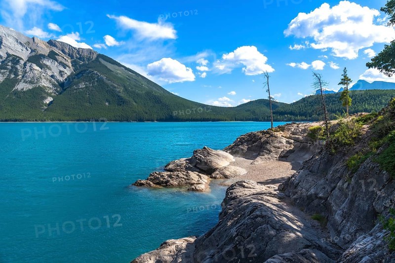 Breathtaking turquoise waters of lake minnewanka reflecting the majestic canadian rockies under a vibrant blue sky with scattered clouds in banff national park, alberta