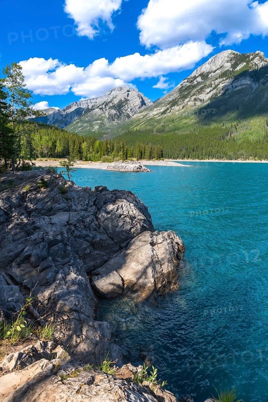 Breathtaking turquoise waters of lake minnewanka reflecting majestic rocky mountains under a vibrant blue sky with fluffy clouds in banff national park