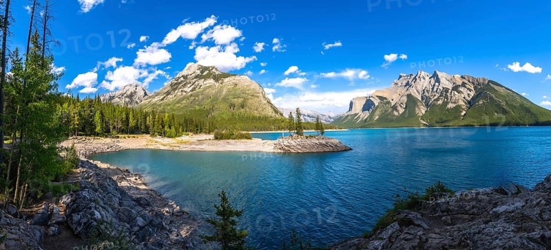 Sunlight illuminating the turquoise waters of lake minnewanka, reflecting surrounding mountains and a small island of evergreen trees in banff national park