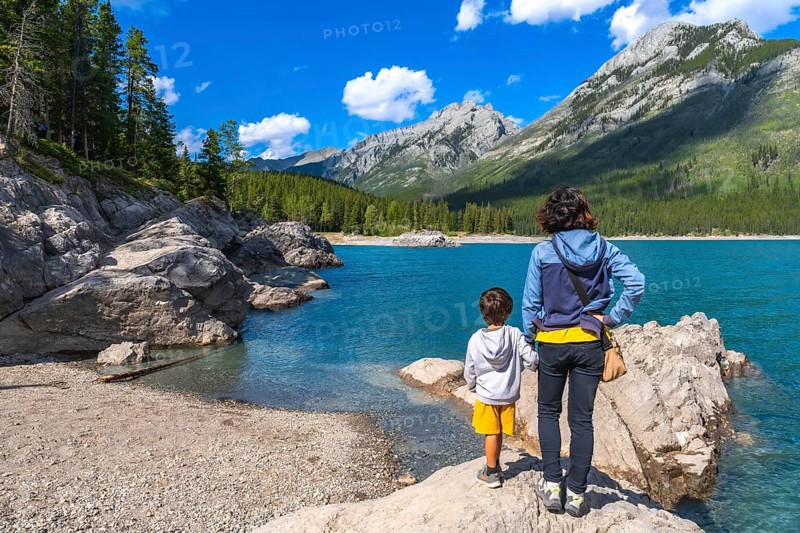 Mother and son standing on a rock, admiring the stunning turquoise waters of lake minnewanka, surrounded by the majestic canadian rockies on a sunny day