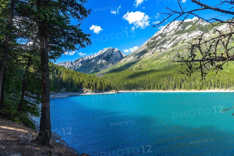 Sunlight illuminating the turquoise waters of lake minnewanka reflects the majestic canadian rockies and lush evergreen forests in banff national park, alberta