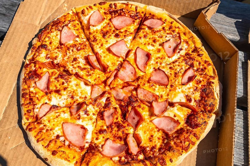 Sliced pizza with ham and melted cheese inside a cardboard box is waiting to be eaten outdoors, creating a perfect image for food delivery services or restaurants