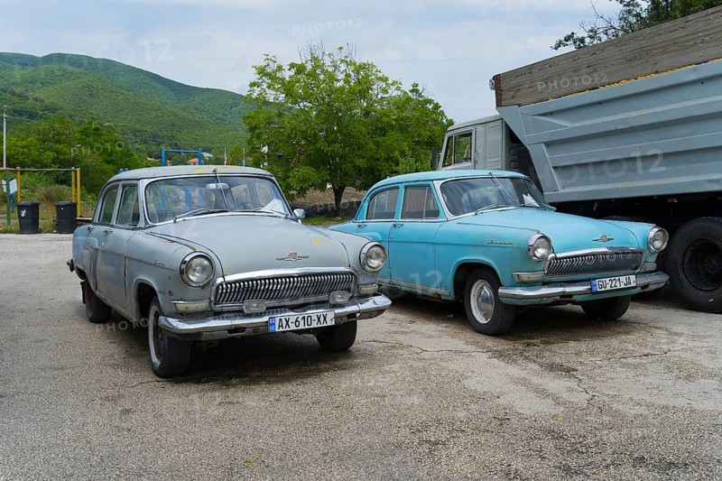 Two vintage cars are parked in a parking lot in front of a hilly landscape, GAZ M-21 Volga, Georgia