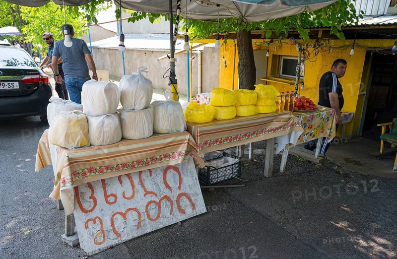 Market stand with various types of cheese and products under trees at a busy market selling cheese, tomatoes and oil, Badiauri, Kakheti region, Georgia