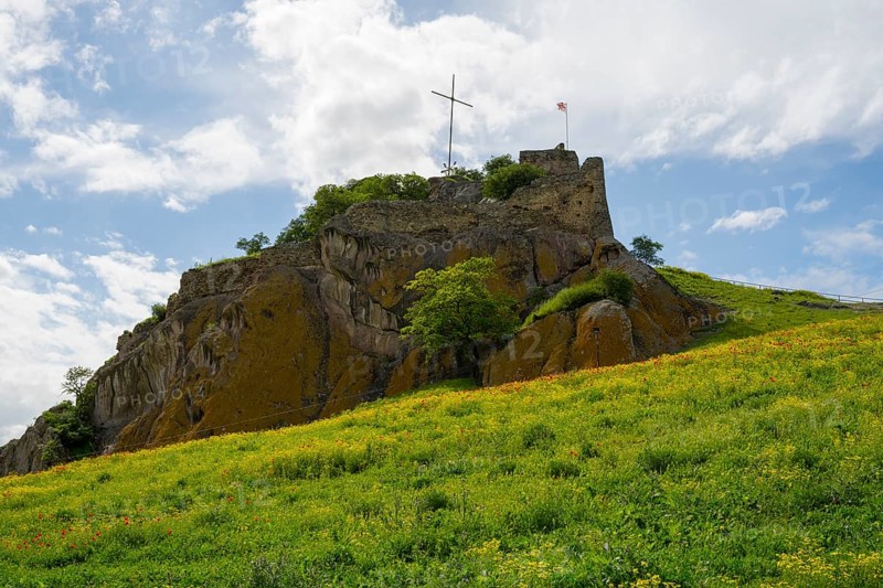 An old castle on a green hill under cloudy sky with a cross on top, Kveshi fortress, Bolnisi, Bolnissi, Lower Kartli region, Georgia