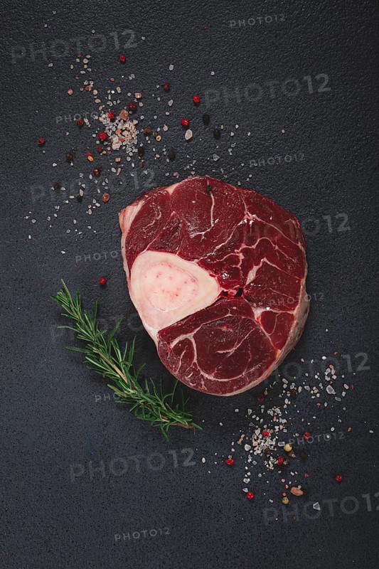 A shank on the bone, raw meat for ossobuco, on the table, with a branch of rosemary, top view, no people