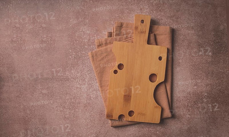 Wooden cutting board, rectangular with handle, cheese shape with holes, on a kitchen towel, top view, food background, no people