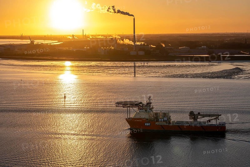 Offshore workship EDT Prometheus arrives at the mouth of the Weser, in the background the Kronos Titan chemical plant, a leading global manufacturer of titanium dioxide, in Nordenham, Bremerhaven, sunset, Germany