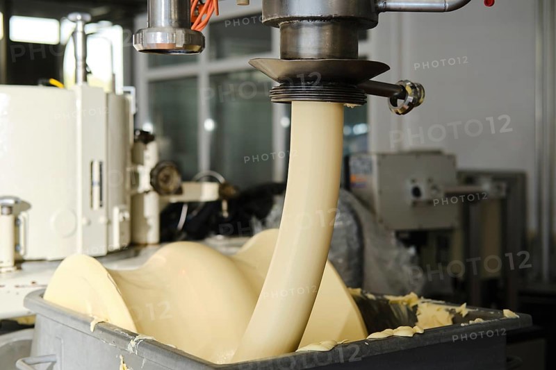 Automated food production machine dispensing butter into container in industrial manufacturing facility