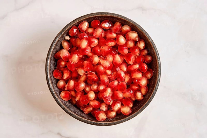 A bowl is filled with bright red pomegranate seeds. These seeds are fresh and cut from the fruit. They are ready to be used in dishes or eaten as a snack