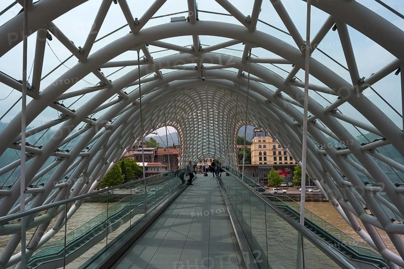 View through the modern glass bridge across a river with urban surroundings, Peace Bridge, Tbilisi, Tbilisi, Kura River, Georgia