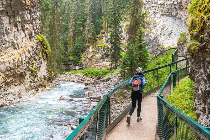Female tourist with a backpack walking along a metal catwalk, taking in the scenic views of johnston canyon and the turquoise bow river in banff national park, alberta