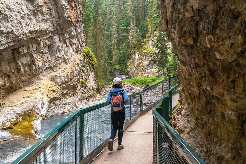 Female tourist with backpack walking on a metal catwalk enjoying the scenic view of johnston canyon and the bow river in banff national park, alberta, canada, during summer