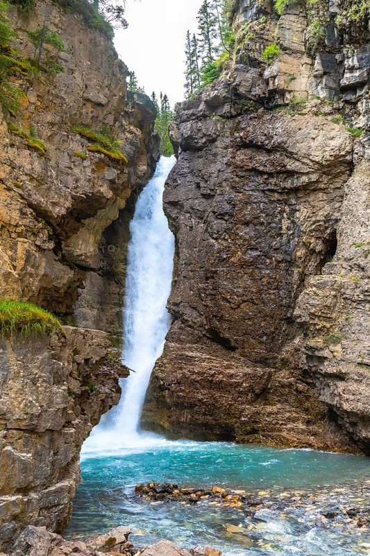 Breathtaking waterfall cascading into a vibrant turquoise pool, surrounded by rugged cliffs and lush greenery in johnston canyon, banff national park, alberta