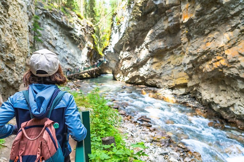 Female tourist with a backpack admiring the turquoise waters of bow river flowing through johnston canyon in banff national park on a summer day