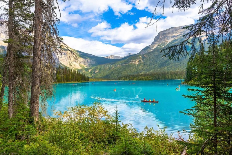 Tourists are canoeing on the turquoise waters of emerald lake, surrounded by lush vegetation and the imposing canadian rockies in banff national park, alberta, under a bright summer sky