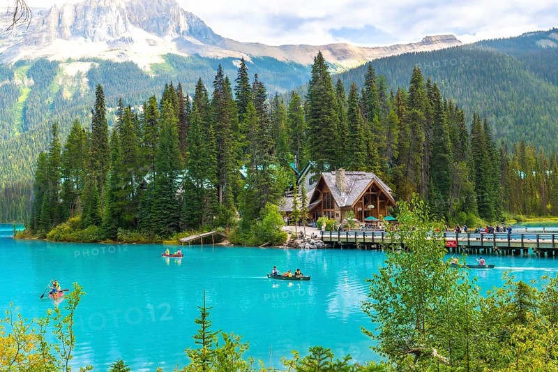 Tourists are canoeing on the turquoise waters of emerald lake with a beautiful wooden lodge and the canadian rockies in the background, in banff national park, alberta, canada