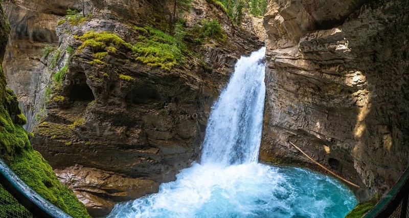 Sunlight illuminating the vibrant turquoise pool at the base of a cascading waterfall in johnston canyon, banff national park, showcases breathtaking natural beauty
