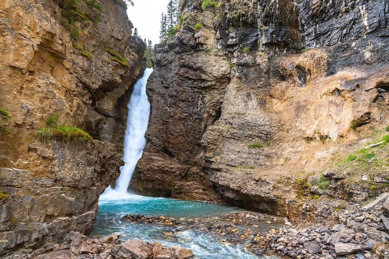 Cascading waterfall flowing into a vibrant turquoise pool in johnston canyon, surrounded by rugged cliffs and lush greenery in banff national park