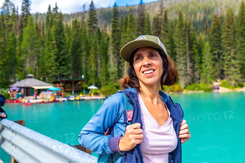 Female hiker wearing a baseball cap and backpack standing near the turquoise waters of emerald lake, admiring the scenic beauty of yoho national park in the canadian rockies, british columbia