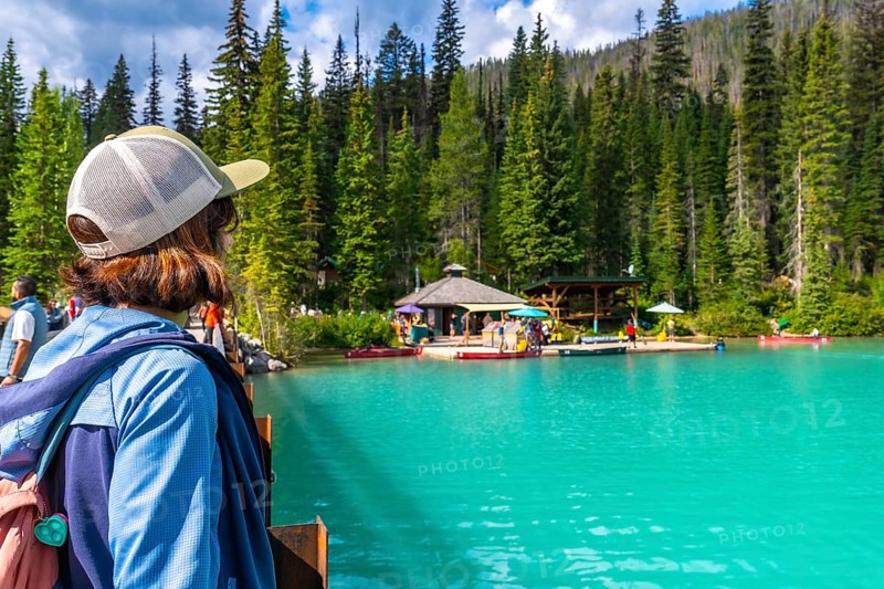 Tourist standing on a bridge admires the turquoise waters of emerald lake, surrounded by lush forests and a boat dock in banff national park, a breathtaking natural wonder in the canadian rockies