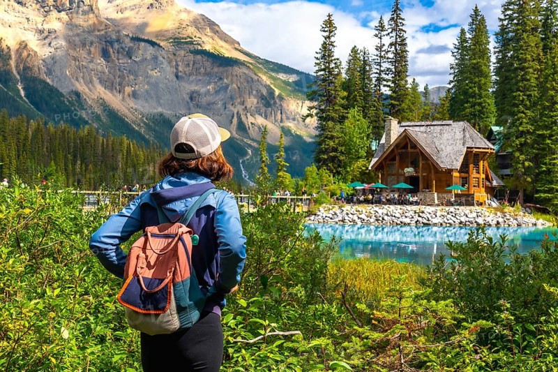 Tourist with a backpack is enjoying the breathtaking view of emerald lake and its charming wooden lodge nestled amidst the stunning canadian rockies in banff national park, alberta
