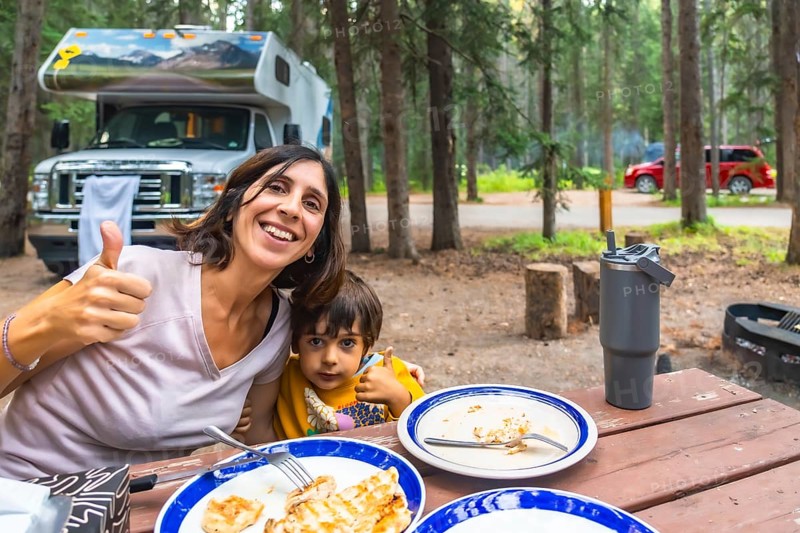 Mother and child showing thumbs up while having lunch at their campsite in banff national park, canadian rockies, with their campervan in the background