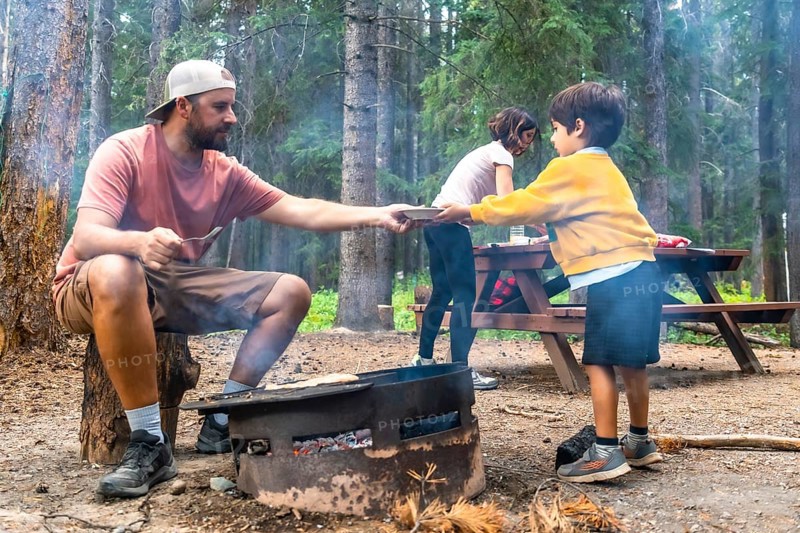 Father serving food to children at campsite, cooking on campfire in banff national park, canadian rockies, alberta, enjoying outdoor lifestyle during summer vacation