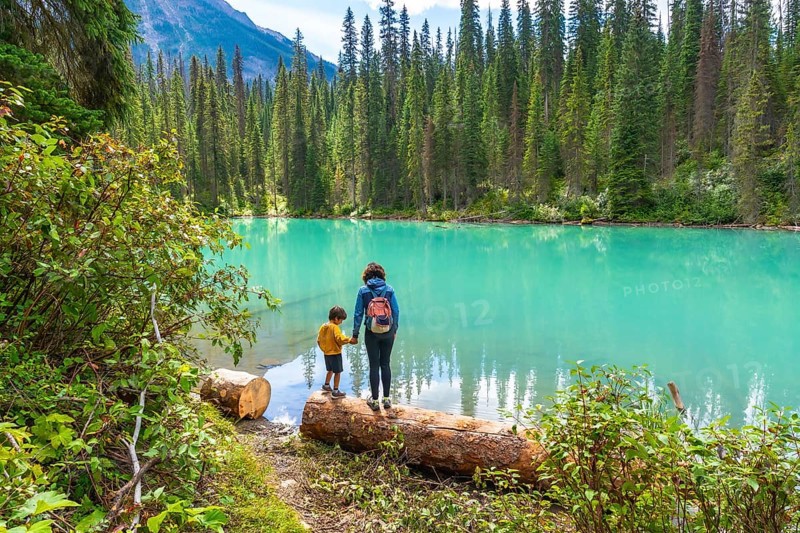Mother and son holding hands on a log, enjoying the stunning turquoise waters of emerald lake, surrounded by lush forests and mountain peaks in banff national park