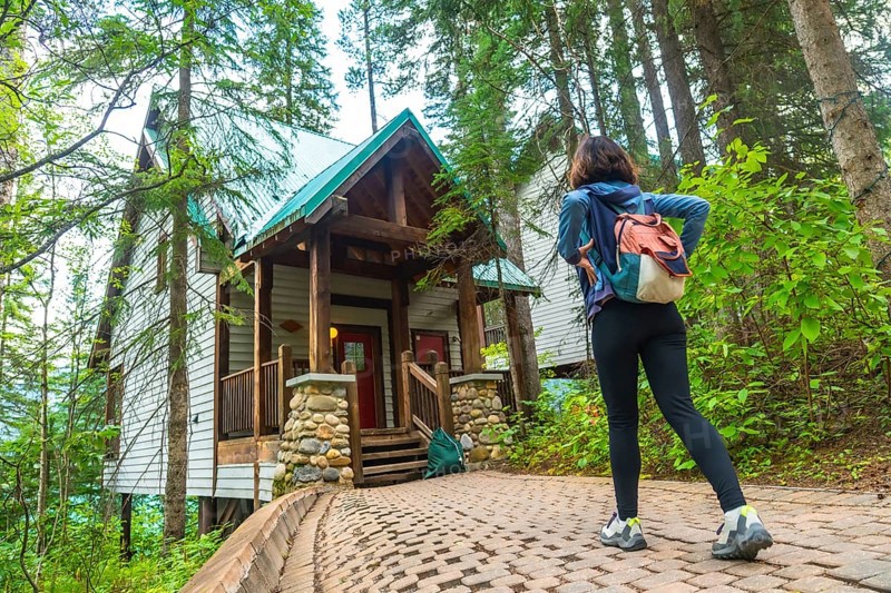 Female tourist with backpack walking on a paved path. Admiring a wooden cabin in the forest near emerald lake in banff national park. Yoho national park. British columbia. Canada. During a summer day