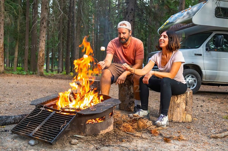Tourists roasting marshmallows over a cozy campfire near their campervan, surrounded by the breathtaking beauty of banff national park and the majestic canadian rockies