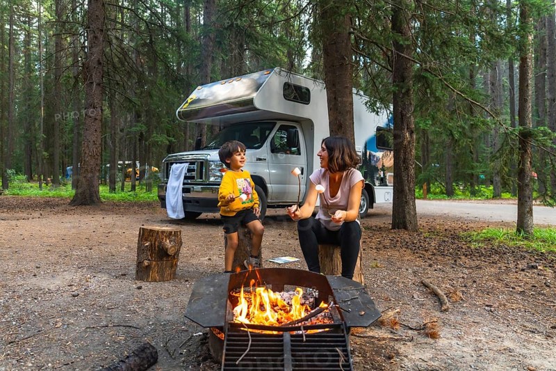 Mother and son roasting marshmallows over campfire near their camper van, enjoying a camping trip in the beautiful wilderness of banff national park, canadian rockies, alberta, canada