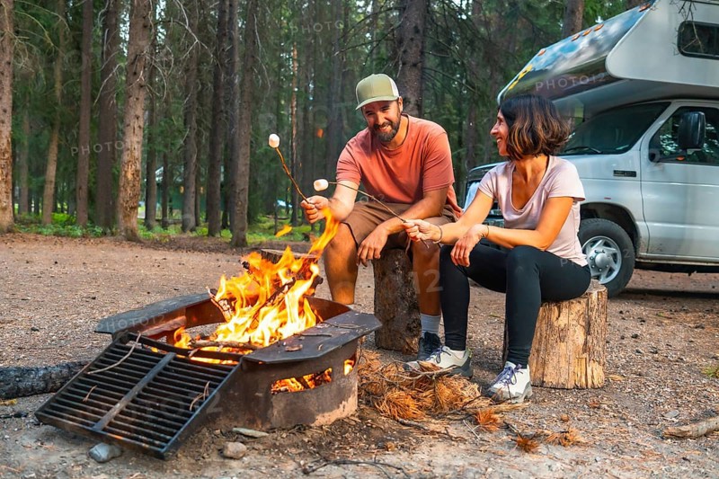 Tourists are roasting marshmallows over a campfire near their campervan in a campsite in banff national park, enjoying a relaxing evening in the canadian rockies