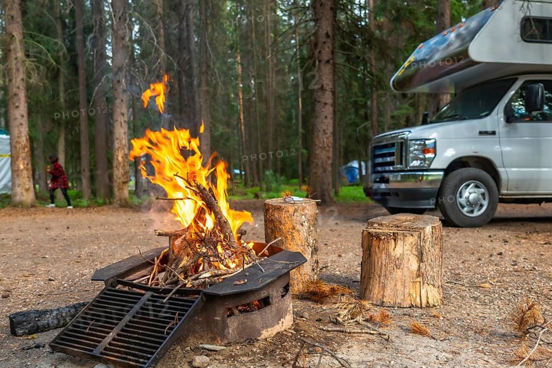 Warm fire glowing in a campsite fire pit beside a camper van in banff national park, alberta, surrounded by a coniferous forest and a tent, creating a cozy atmosphere