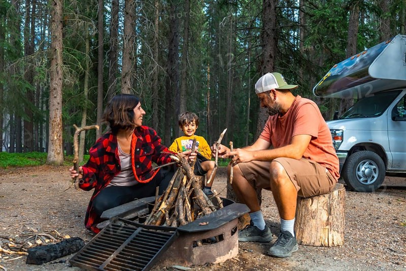 Family enjoying camping in the canadian rockies, preparing campfire next to their campervan in banff national park, alberta, during a sunny summer day