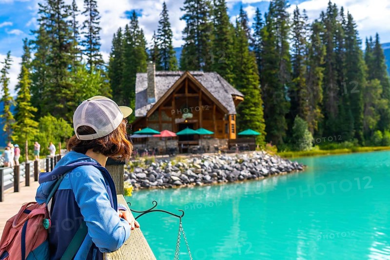 Female hiker admiring the turquoise waters of emerald lake and its charming lodge, nestled among lush pine forests in banff national park, alberta, canada