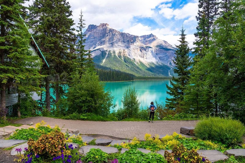 Tourist with a backpack admiring the breathtaking turquoise waters of emerald lake and the imposing mount burgess, surrounded by lush vegetation and a wooden cabin in banff national park