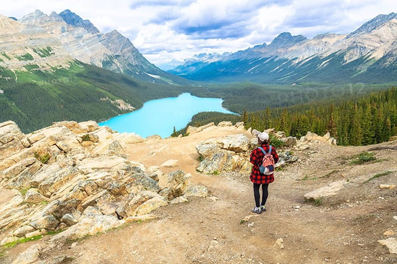 Female hiker admiring the stunning turquoise hues of peyto lake, surrounded by majestic mountains and lush valleys in banff national park, alberta, within the canadian rockies