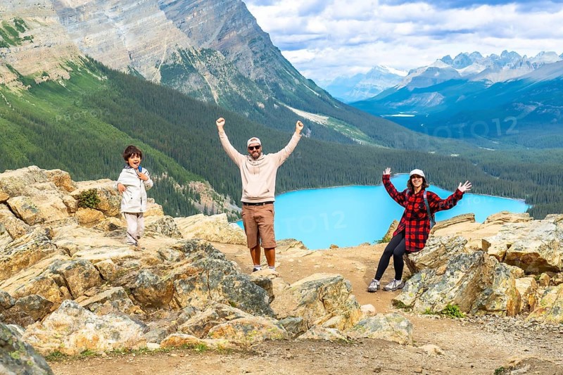 Tourists raising their arms in excitement while admiring the stunning turquoise peyto lake from a rocky viewpoint in banff national park, surrounded by majestic mountains