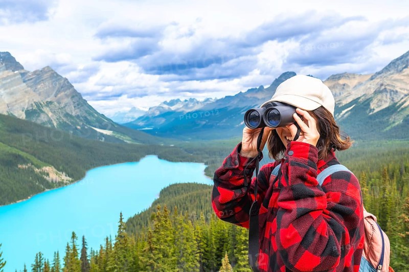 Female hiker using binoculars, admiring the scenic turquoise waters of peyto lake and the majestic mountains in banff national park, alberta, canada