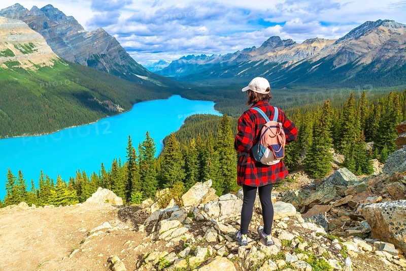 Female hiker wearing a backpack, standing on a rocky viewpoint and admiring the stunning turquoise waters of peyto lake amidst the canadian rockies in banff national park