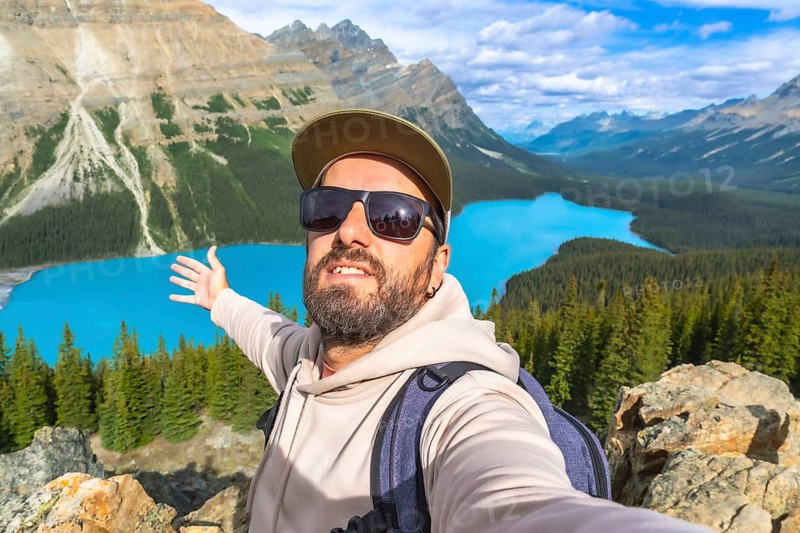 Hiker taking a selfie with outstretched arms, embracing breathtaking turquoise waters of peyto lake, surrounded by majestic mountains and lush forests in banff national park