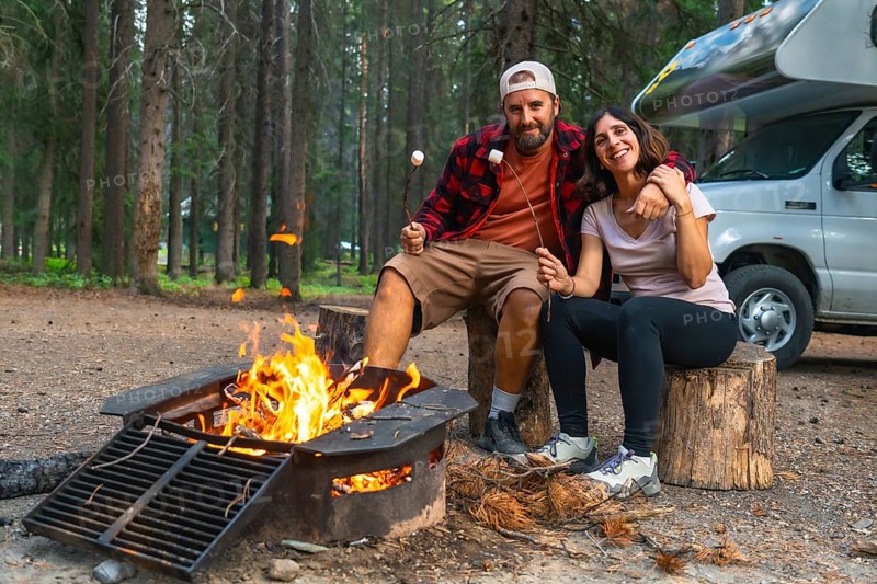 Tourists roasting marshmallows in banff national park, alberta, enjoying a cozy evening by the campfire next to their campervan, surrounded by the serene beauty of the canadian rockies