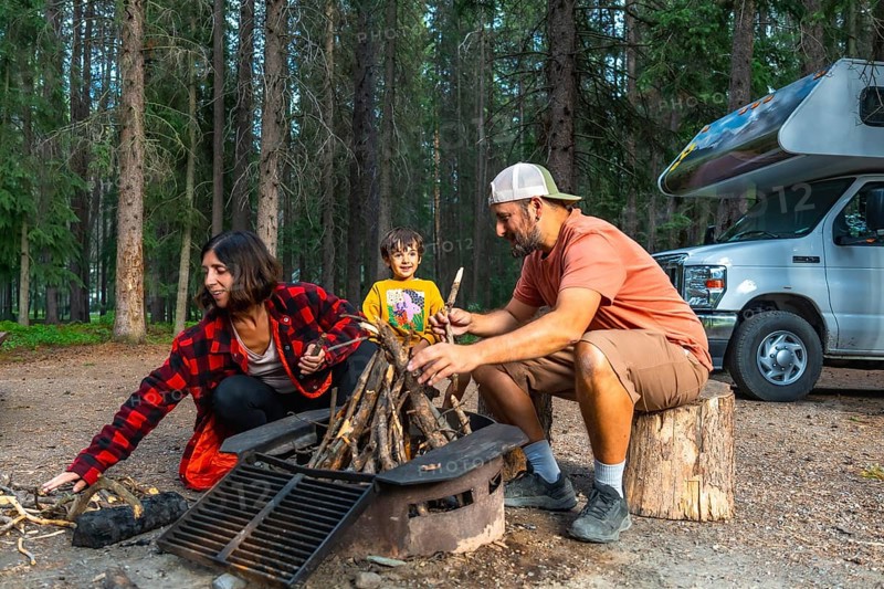 Family enjoying a delightful camping trip, gathering around a crackling campfire beside their cozy camper van in banff national park, surrounded by the stunning canadian rockies of alberta, canada