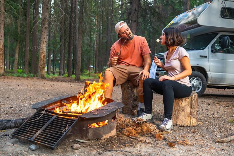 Tourists roasting marshmallows in a campfire near their campervan, enjoying a relaxing evening in the woods of banff national park in the canadian rockies, alberta