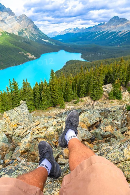 Hiker resting on a rocky mountain top, soaking in the stunning panoramic view of turquoise peyto lake and the majestic canadian rockies in banff national park
