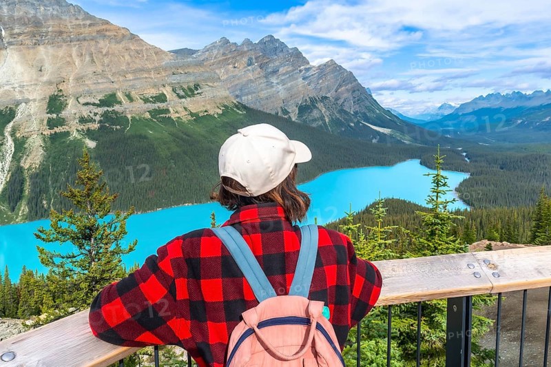 Female tourist with backpack and baseball cap enjoying breathtaking panoramic view of turquoise peyto lake and surrounding canadian rockies in banff national park. Alberta. Canada. During summer day